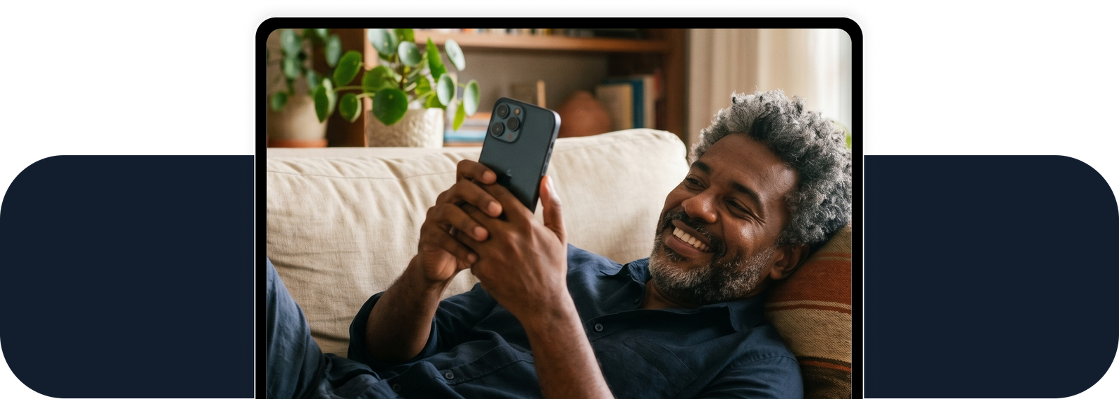 Homem sorridente usando celular no sofá, com plantas ao fundo.