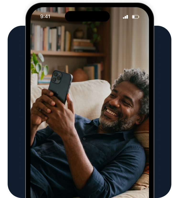 Homem sorrindo enquanto usa um smartphone em um sofá aconchegante.